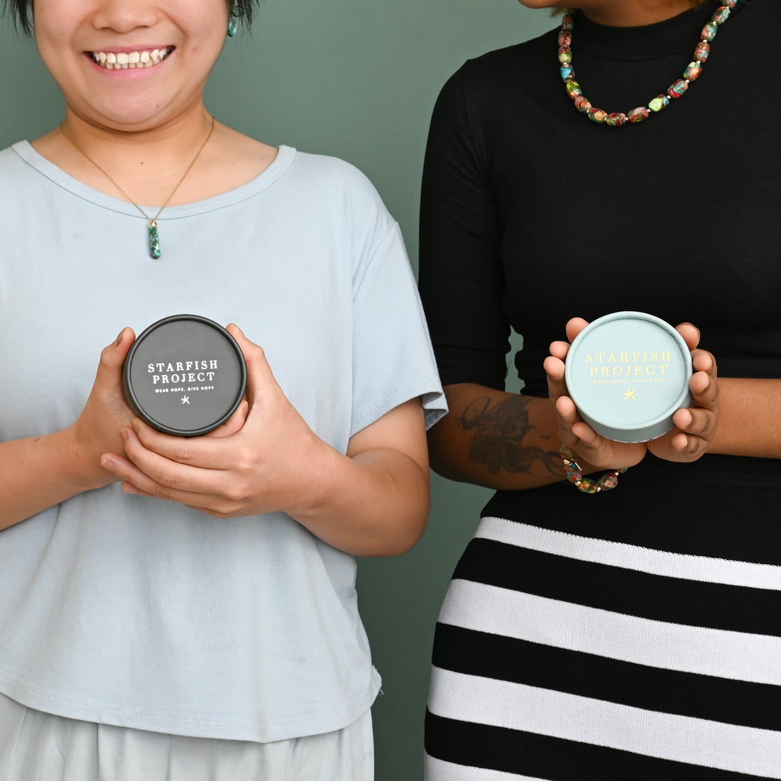 Two smiling women holding Starfish Project jewelry boxes in grey and mint