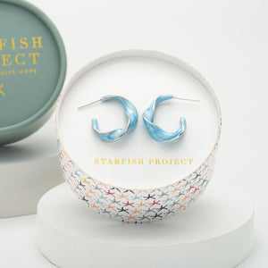 White gold and sky blue enamel hoop earrings by Starfish Project in a sound box with a colorful starfish pattern, ethical jewelry and a meaningful gift for women.
