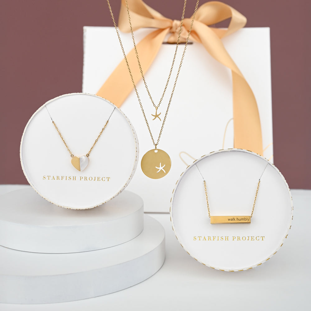 Gold necklaces on display with luxe gold & white Starfish Project gift packaging.  