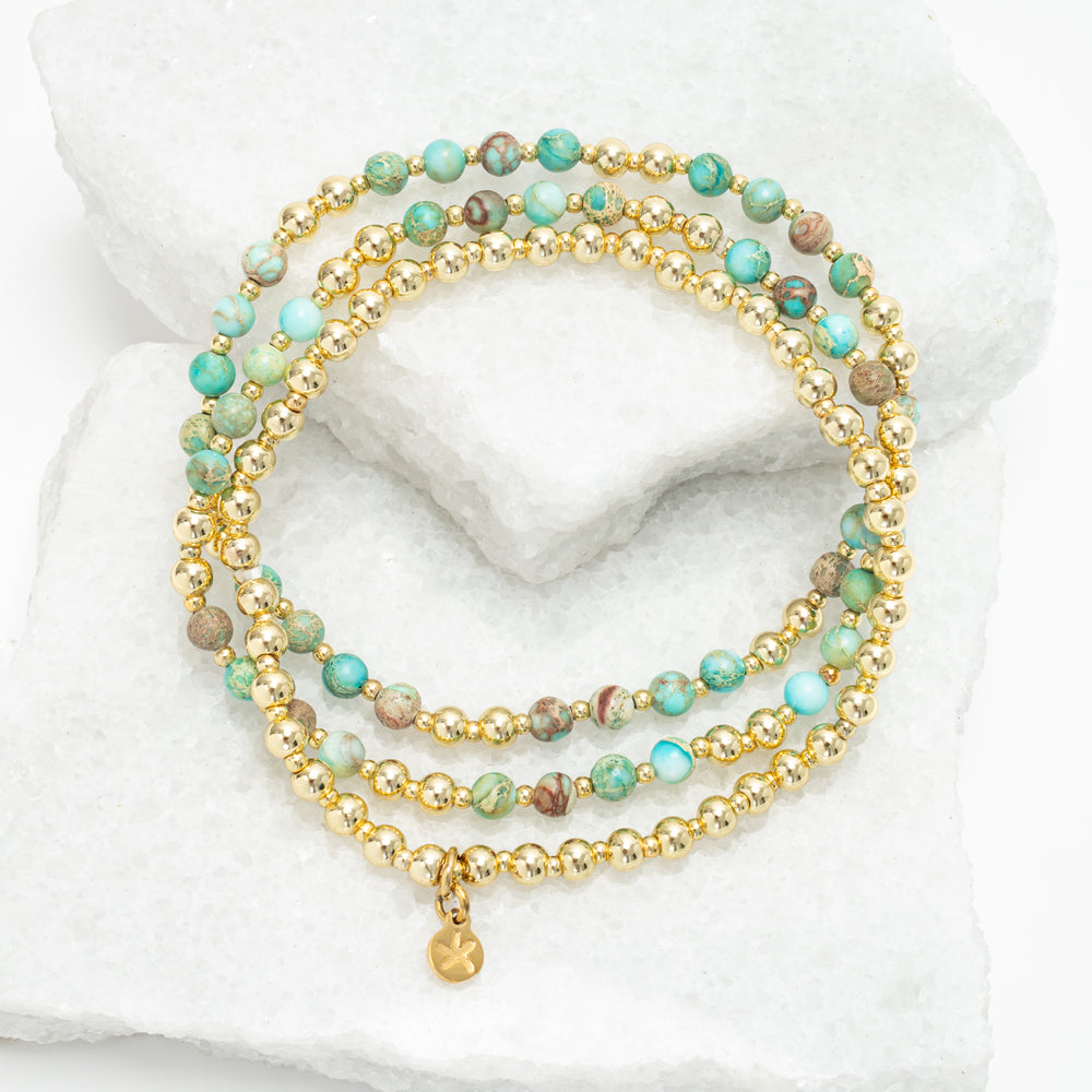 Stack of beaded bracelets with gold accents on a white marble surface, 18k gold plated beads, gold bracelet, sustainable fair trade women's jewelry