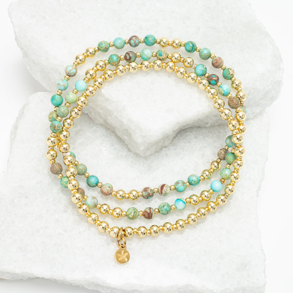 Stack of beaded bracelets with gold accents on a white marble surface, 18k gold plated beads, gold bracelet, sustainable fair trade women's jewelry