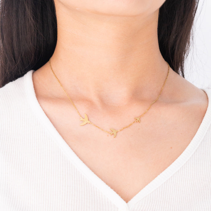 Woman wearing golden bird necklace, sparrow pendant necklace, simple gold necklace with birds, fair trade groups